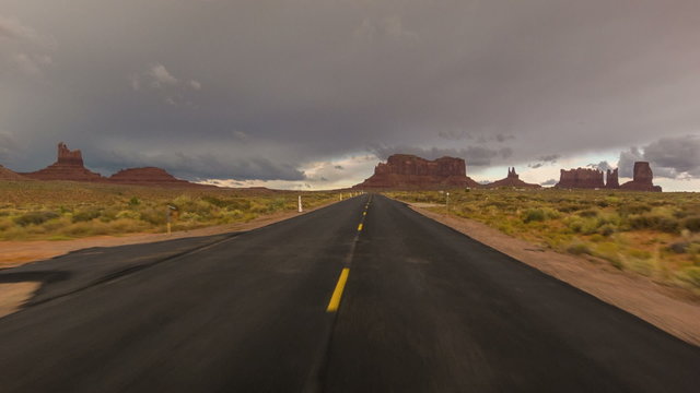 Driving USA: Dramatic point of view POV shot of empty lonely road and stormy skies over Monument Valley, Arizona Utah
