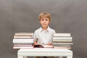 Young boy reading  at a table full of books