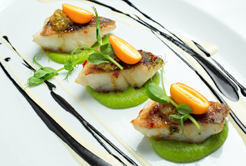 Delicious fish served on white dish, decorated with salad and sauce