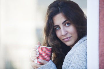 Young beautiful woman drinking coffee and looking out of the window