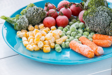 frozen vegetables: broccoli, cherry tomatoes, corn, pea, carrot on blue plate