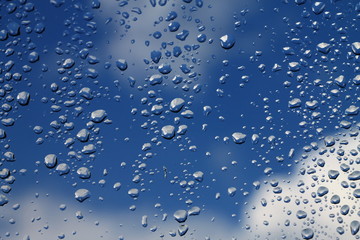 Rain drops on window with blue cloudy sky in background