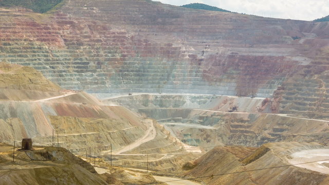 Wide angle time-lapse of open pit copper mine. Mountain carved into terraces for mining, with dump trucks driving and speeded up clouds