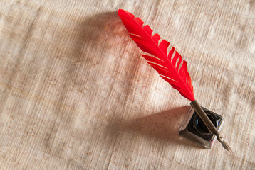 Red quill pen and black inkwell on a papyrus leaf