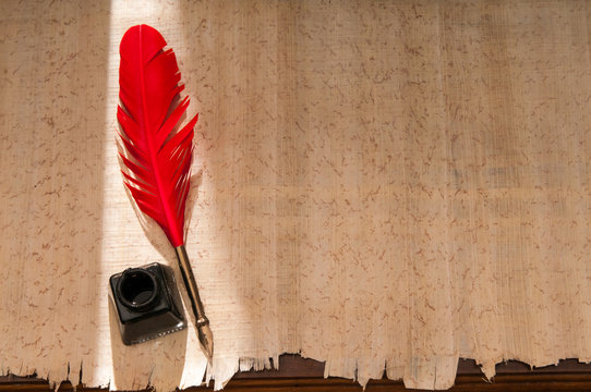 Red quill pen and black inkwell on a papyrus leaf