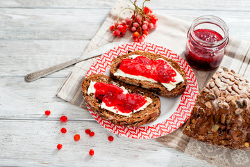 light breakfast or lunch , sandwiches of rye bread with butter , raspberry jam , berries and black tea on the wooden background 
