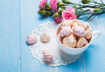 Meringues in the cup and pink flowers on the table close-up