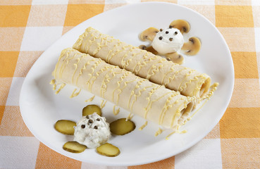 Two crepes with savory filling served on a white plate with marinated mushrooms, pickled cucumber, sour cream and mayonnaise.