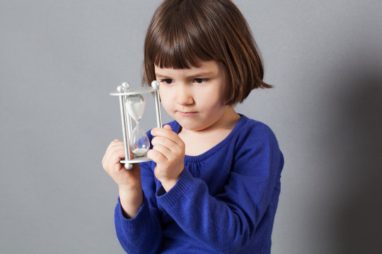 kid time concept - serious female preschooler enjoying learning about time, holding an hour glass for insouciance and future,studio shot