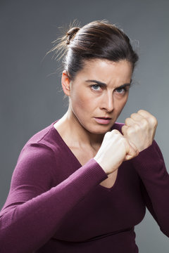 female self-defense concept - angry 30s woman countering violence in fighting and showing her fists,studio shot