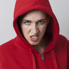 female threat concept - rebellious 20s girl wearing streetwear with hooded sweater expressing hatred and rage,closeup in studio