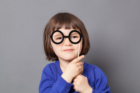 fun kid glasses concept - wise preschool child holding fake black round eyeglasses for playing like adult or dressing up as smart nerd,studio shot