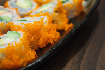 Sushi roll, row of California maki roll sushi with caviar on bla