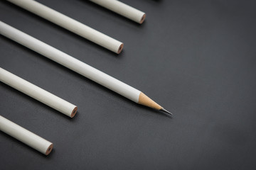 one white pencil among many pencils on black