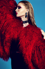 fashion glamor stylish swag young woman model in hipster red fur coat with bright makeup on blue...