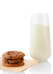 Stack of three homemade chocolate chip cookies on baking paper and glass of milk, isolated on white background