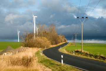 Windräder und Strommast unter dunklen Wolken