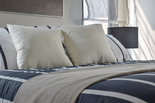 Offwhite and striped pillows on bed with deep blue striped blank