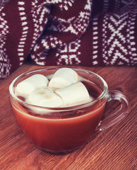 cup of hot cocoa with marshmallow and warm knitted scarf on wood