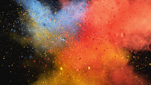Red, yellow and blue powder/particles fly after being exploded against black background. Shot with high speed camera, phantom flex 4K. 4K 30fps. Slow Motion.