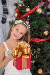 Teenage girl holding Christmas present in front of New Year tree