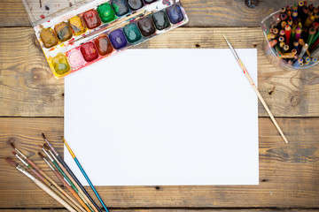 Plastic paint palette with paint and brushes on wooden table