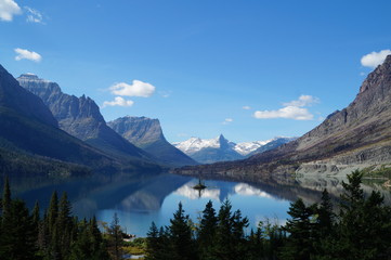 View over a small island in Glacier National Park, USA. The mountains and clouds are reflected in the water.