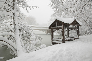 Central Park peaceful winter scene after heavy snowfall. The Bow Bridge and a wooden gazebo are covered by fresh snow at The Lake. Manhattan, New York City