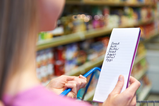 Close Up Of Woman Reading Shopping List In Supermarket