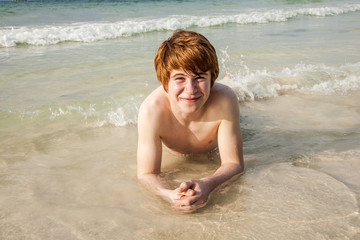 boy  is lying at the beach and enjoying the saltwater with tiny waves and smiles