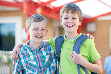 Two Boys Standing Outside School With Book Bags