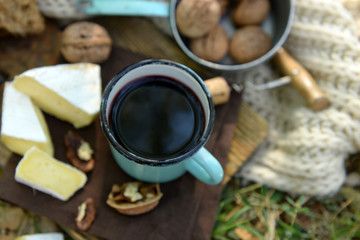 Mug with red wine, delicious cheese and nuts on wooden board outdoors - picnic theme