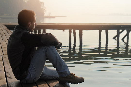 Man sitting on old wooden dock and looking at lake horizon. Thinking, contemplation  relaxing, concentration, loneliness concept