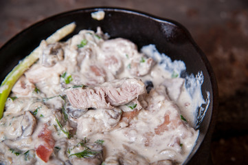 Meat with mushrooms in cream sauce in a pan