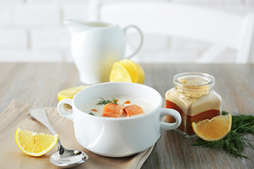 Delicious salmon cream soup on wooden table, which served with sliced lemon and spices