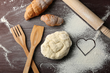 Heart of flour, croissant and  wooden kitchen utensils on gray background