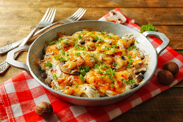 Roasted mushrooms, chicken and cheese gratin in pan, on wooden background