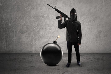 Man with bomb and holding rifle standing against gray background