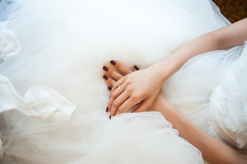 Hands of the bride with a wedding ring lying on the dress