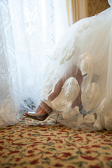 Fototapeta na wymiar Legs of the bride in silver shoes visible from under the dress
