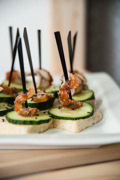 Snack on white bread with fried shrimp and cucumber on a skewer