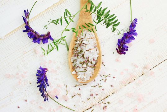 Pink and white bath epsom salt mixture in wooden spoon, fresh and dried aroma herbs. Wooden surface, top view destressing mineral spa background. 
