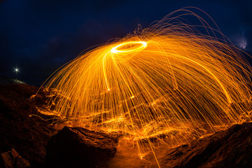 orange light streak dark blue sky rocky beach ,fire steelwool effect technics