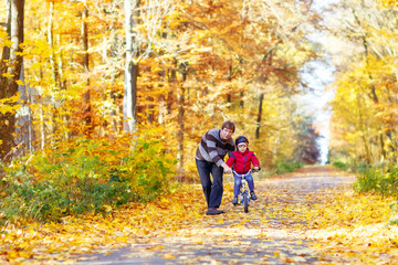 Fototapeta premium Little kid boy and father with bicycle in autumn forest