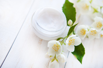 Fototapeta na wymiar Pot of beauty cream with flower petals on white wooden table