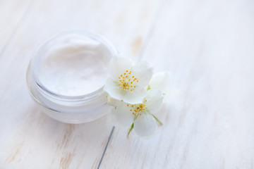 Fototapeta na wymiar Pot of beauty cream with jasmine flower on white wooden table. Close up