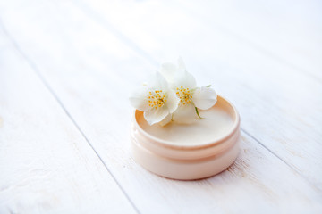 Moisturizing face cream with  jasmine flower on white wooden table. Close up