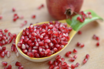 pomegranate grains in yellow green big spoon with whole pomegranate and few grains on the table