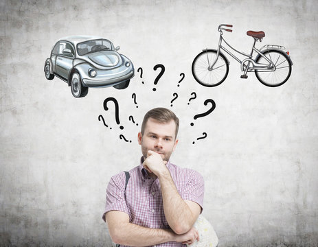A handsome man is trying to chose the most suitable way for travelling or commuting. Two sketches of a car and a bicycle are drawn on the concrete wall. Question marks are around man's head.