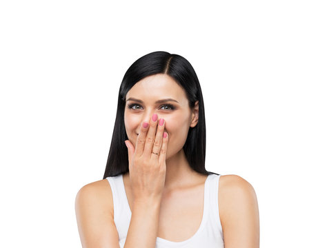 A Portrait Of A Happy Brunette Lady In A White Tank Top Who Is Covering Her Mouth By The Hand. Isolated On White.